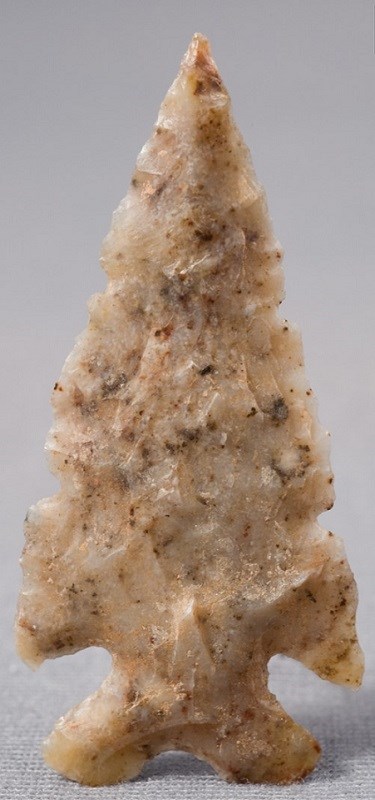 Photo of a solid pale pinkish tan arrowhead against a gray background.