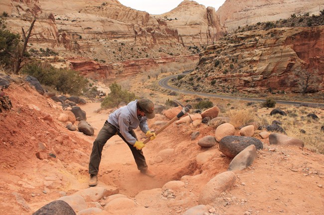 A person with a pickaxe digging on a trail