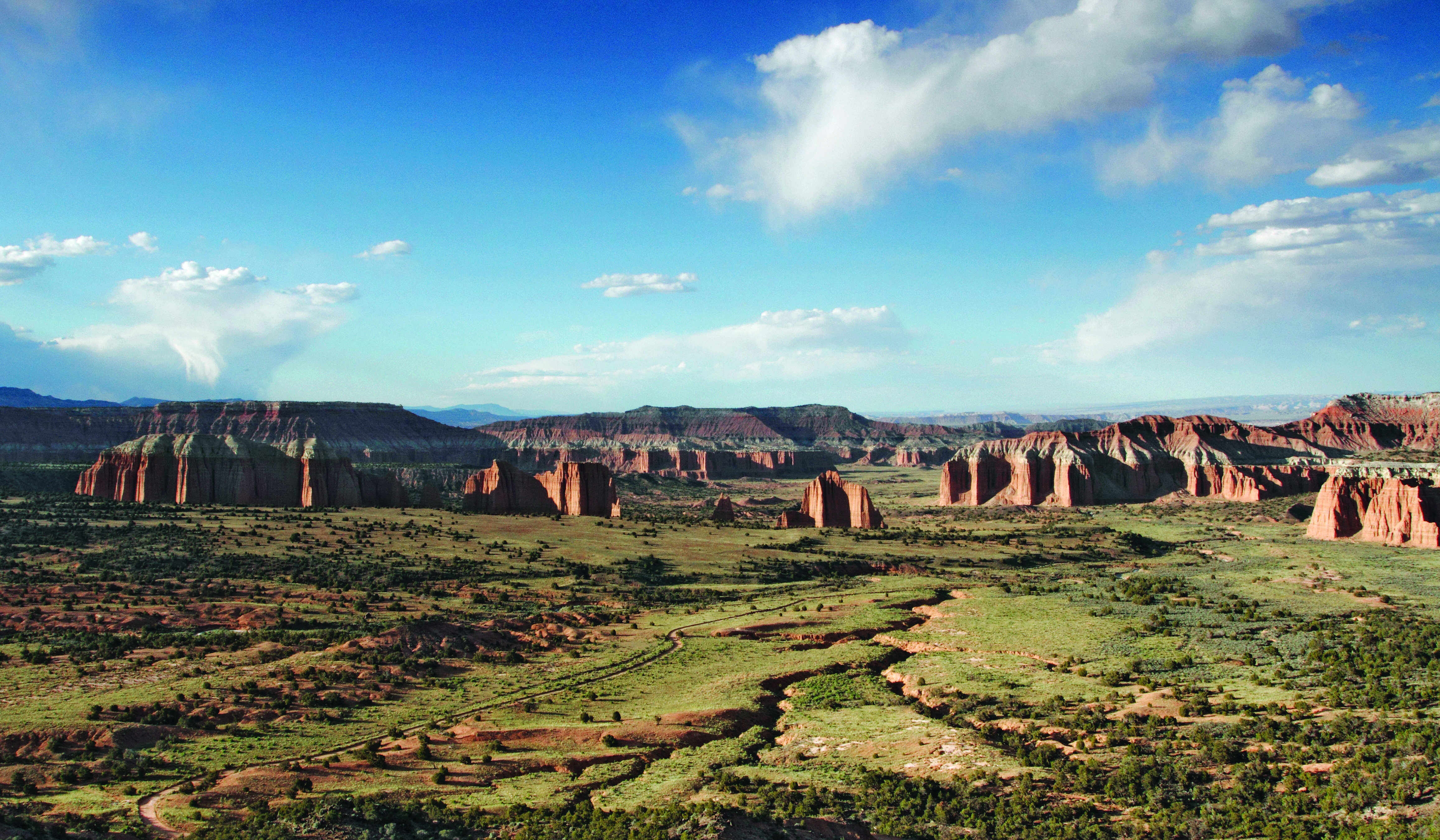 View from above looking down on grassy valley, with large reddish orange rock monoliths protruding out, and blue sky above.