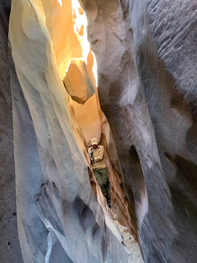 Person squeezing between two narrow canyon walls, with sunlight coming in from above.