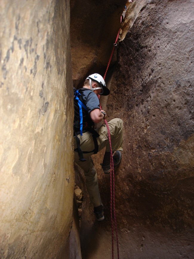 A canyoneer rappels between in a tight squeeze between two sections of rock.
