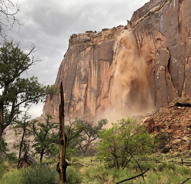 A muddy waterfall cascades over a sheer cliff face.