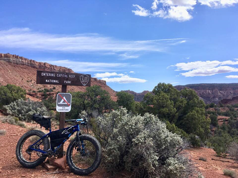 Fat tire bike leaning against wooden sign with scenic red cliffs and blue skies in the background.