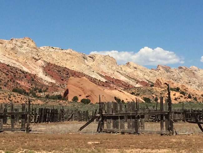 Old, deteriorating wooden fence with colorful rock cliffs and blue sky behind.