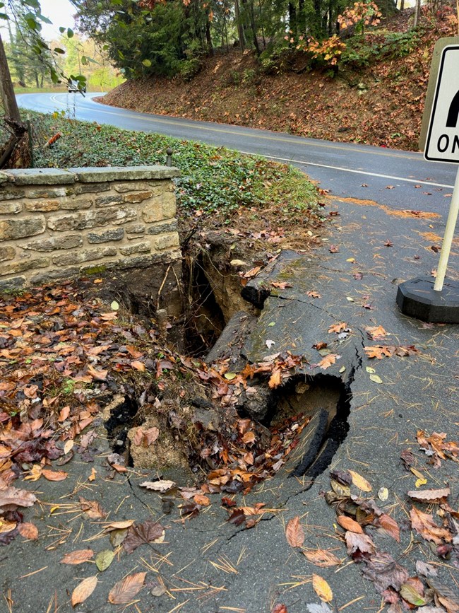 A hole next to a stone wall and in road.