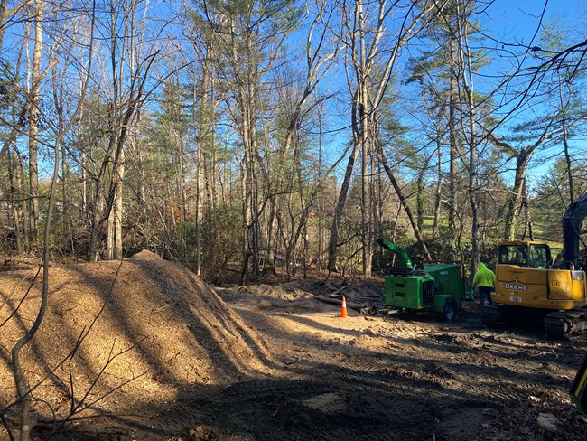 Mound of wood chips with equipment and staff in background.