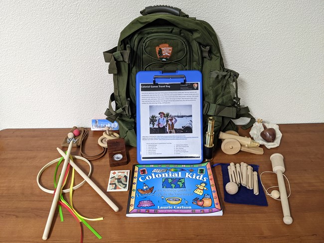 A green NPS backpack with colonial games and a book.