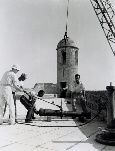 Maintenance workers assist with placing a cannon from crane to gun deck.