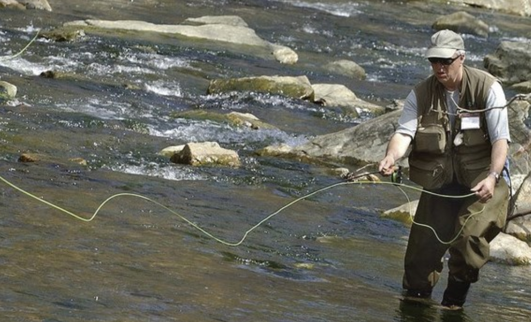 Fly fisherman in waders casting in creek