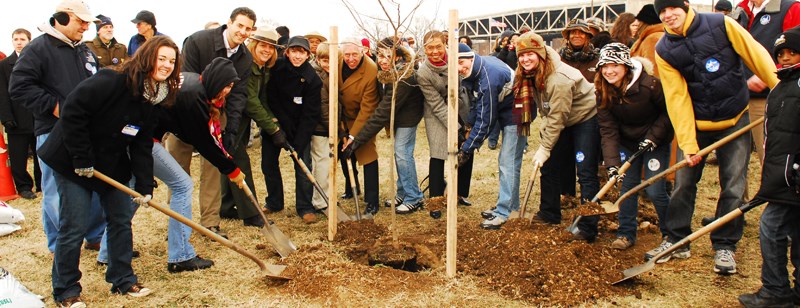 A group of people pose with shovels in the dirt.