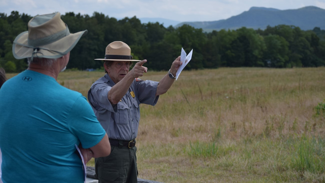 A National Park Service ranger points to something in the distance while leading a tour for visitors.