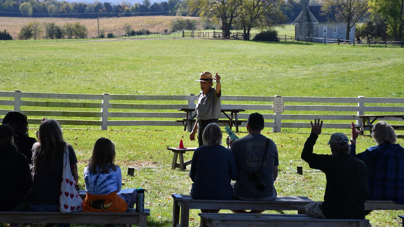 A National Park Service Ranger presents a talk to a group of seated visitors.
