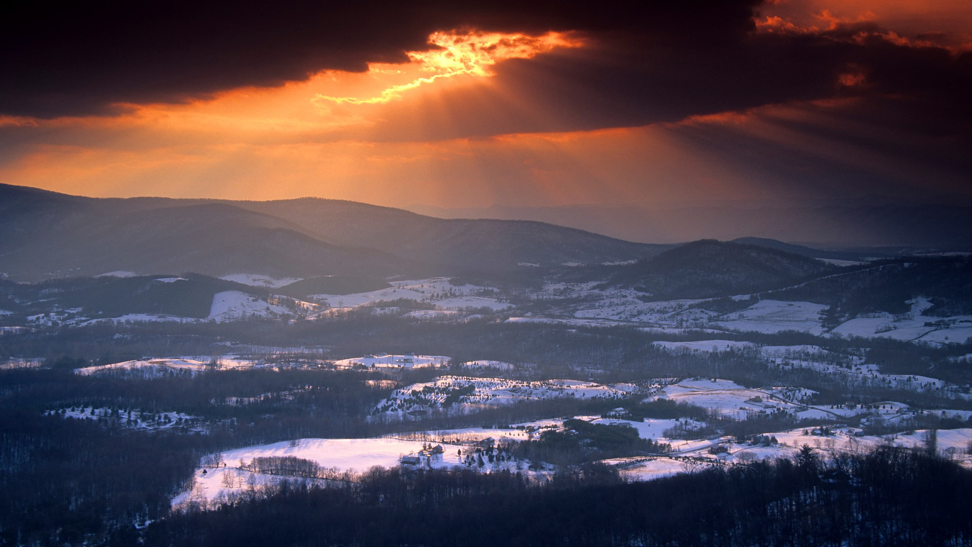 Vibrant orange sunset over snow covered rolling hills in a valley.