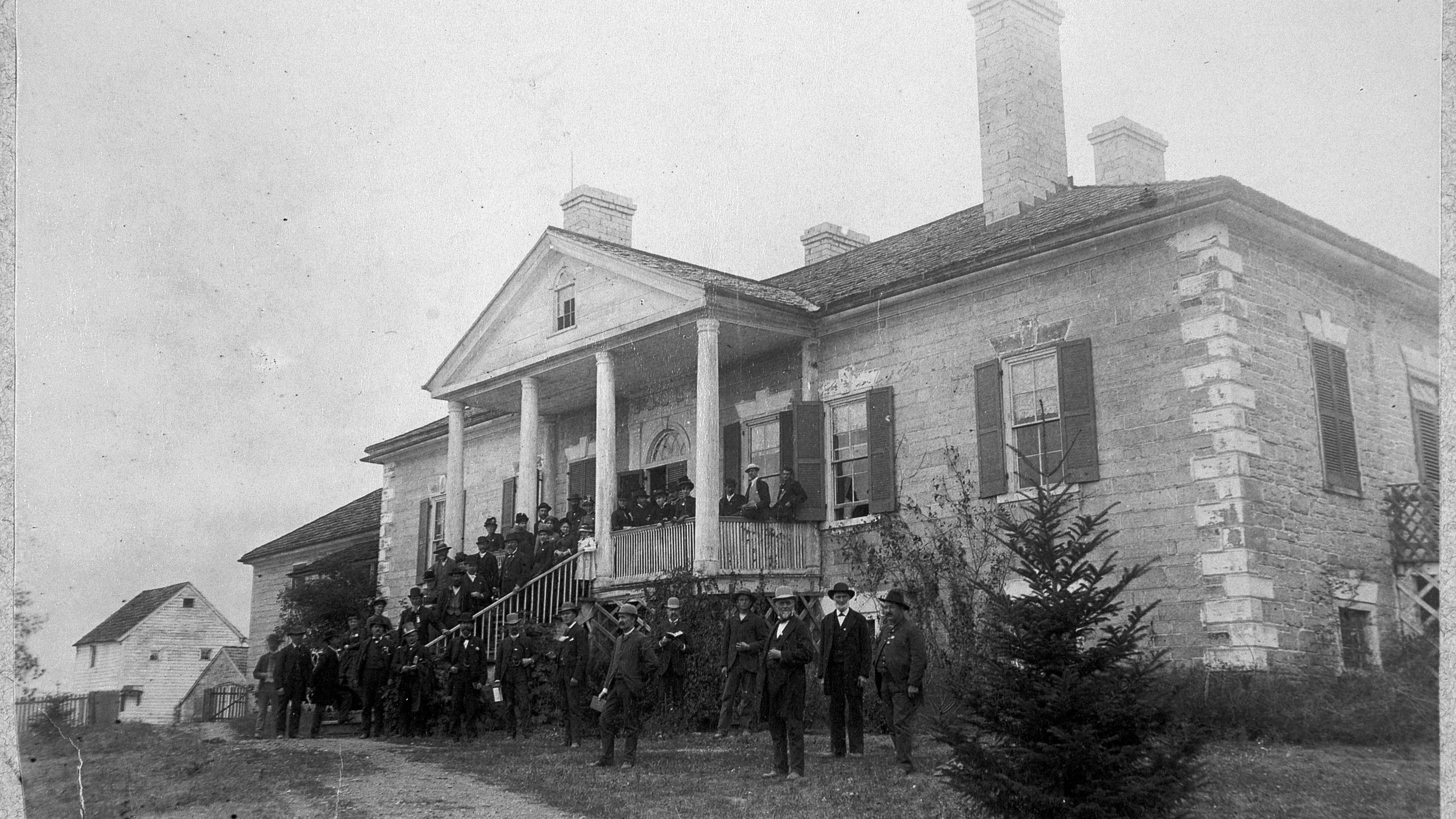 Historic photograph of Civil War veterans gathered on the front porch of a large plantation house.