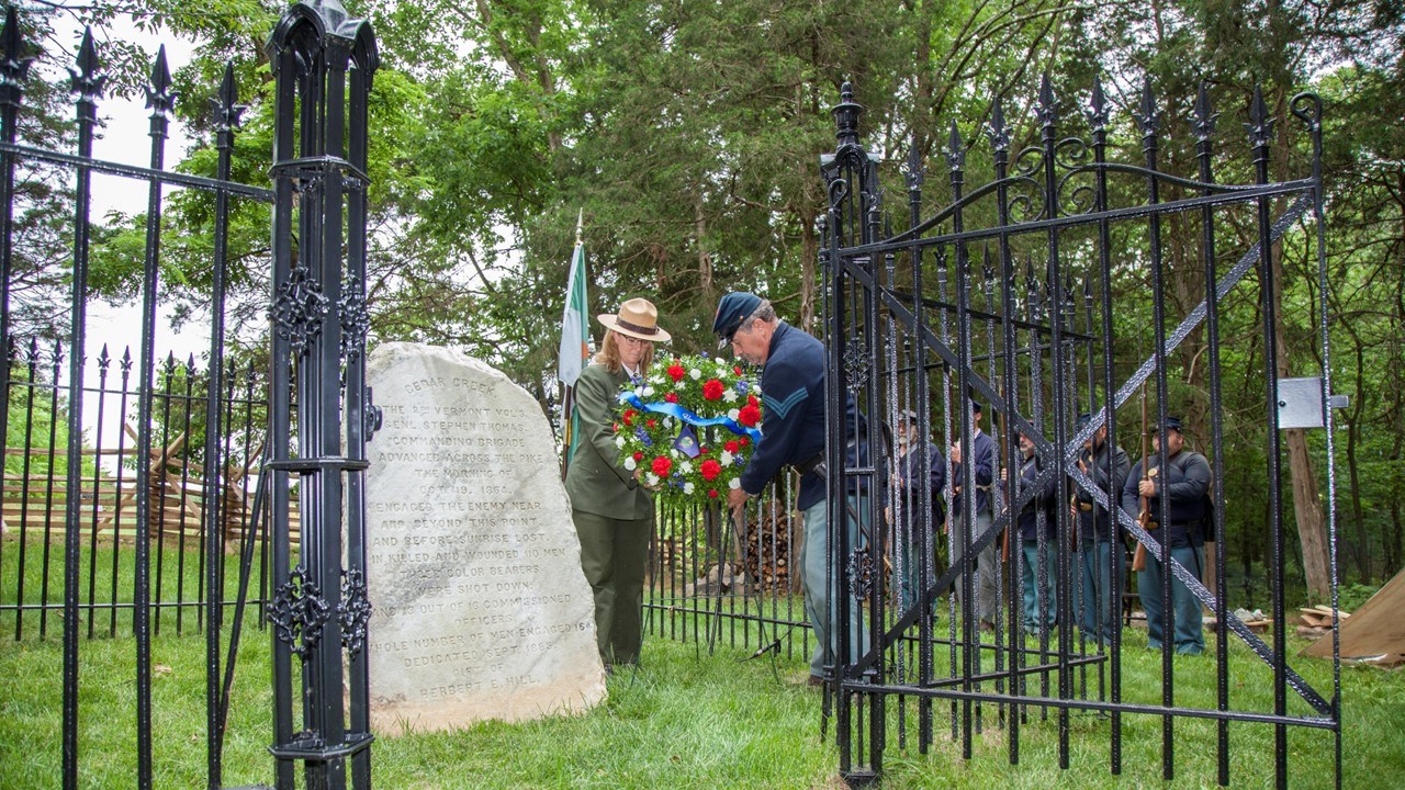 A National Park Service ranger and a Civil War living historian place a wreath next to a marble monument.