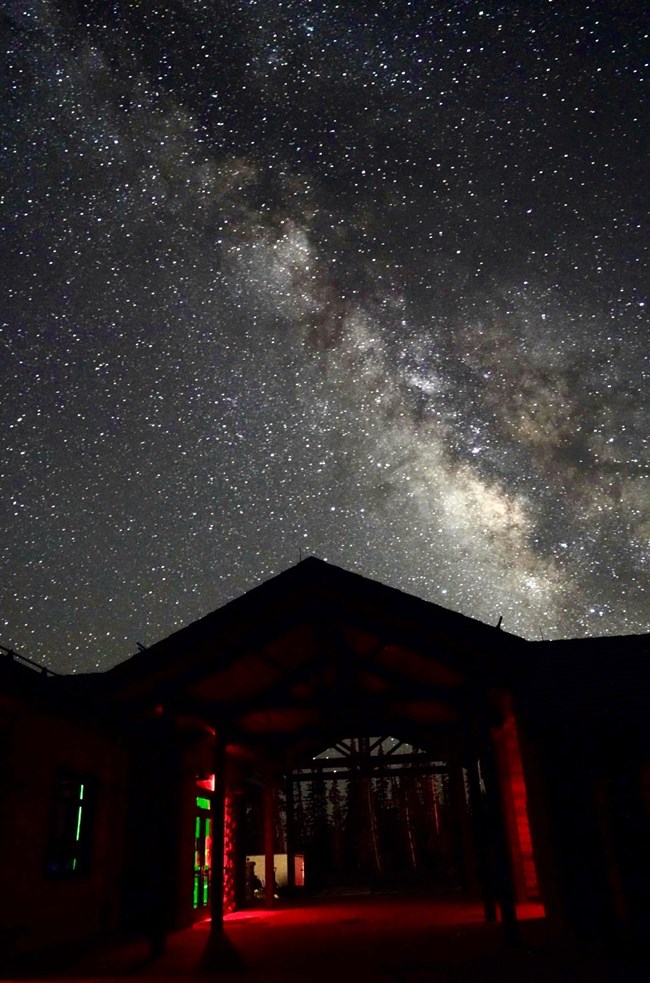 The Cedar Breaks Visitor Center at night under a sky filled with stars, with the Milky Way stretching brightly overhead.