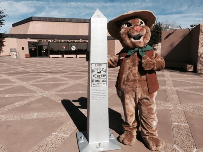 spotted ground squirrel ranger mascot standing next to boundary marker in front of building