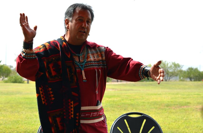 un hombre vestido de camisa tradicional tejida con colores brillantes, quien hace gestos mientras habla
