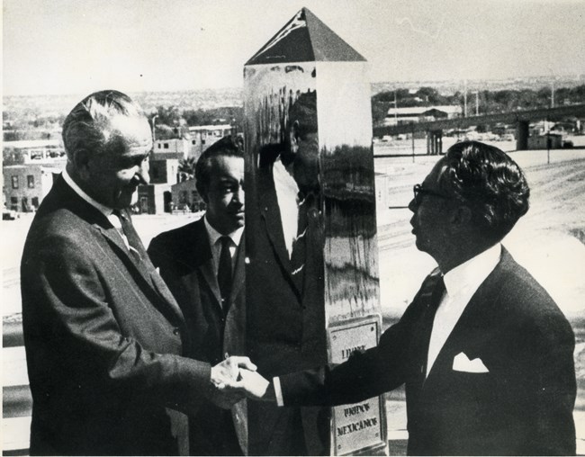 Presidents Lyndon B. Johnson and Gustavo Díaz Ordaz shake hands next to a chrome monument.