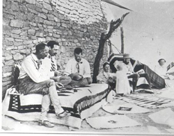 Men and women sitting on a blanket outside a house.