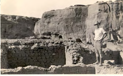 A man standing next to an excavated room of a ruin.