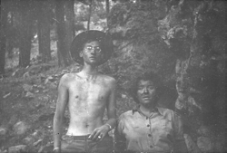 Two people standing next to each other looking at the camera. One is shirtless.