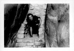 A woman crawling through a small door of a ruins