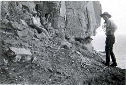 People sitting under a cliff hang with rocks scattered around them