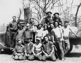Black and white photo of 15 young men in work clothes next to a truck full of saplings