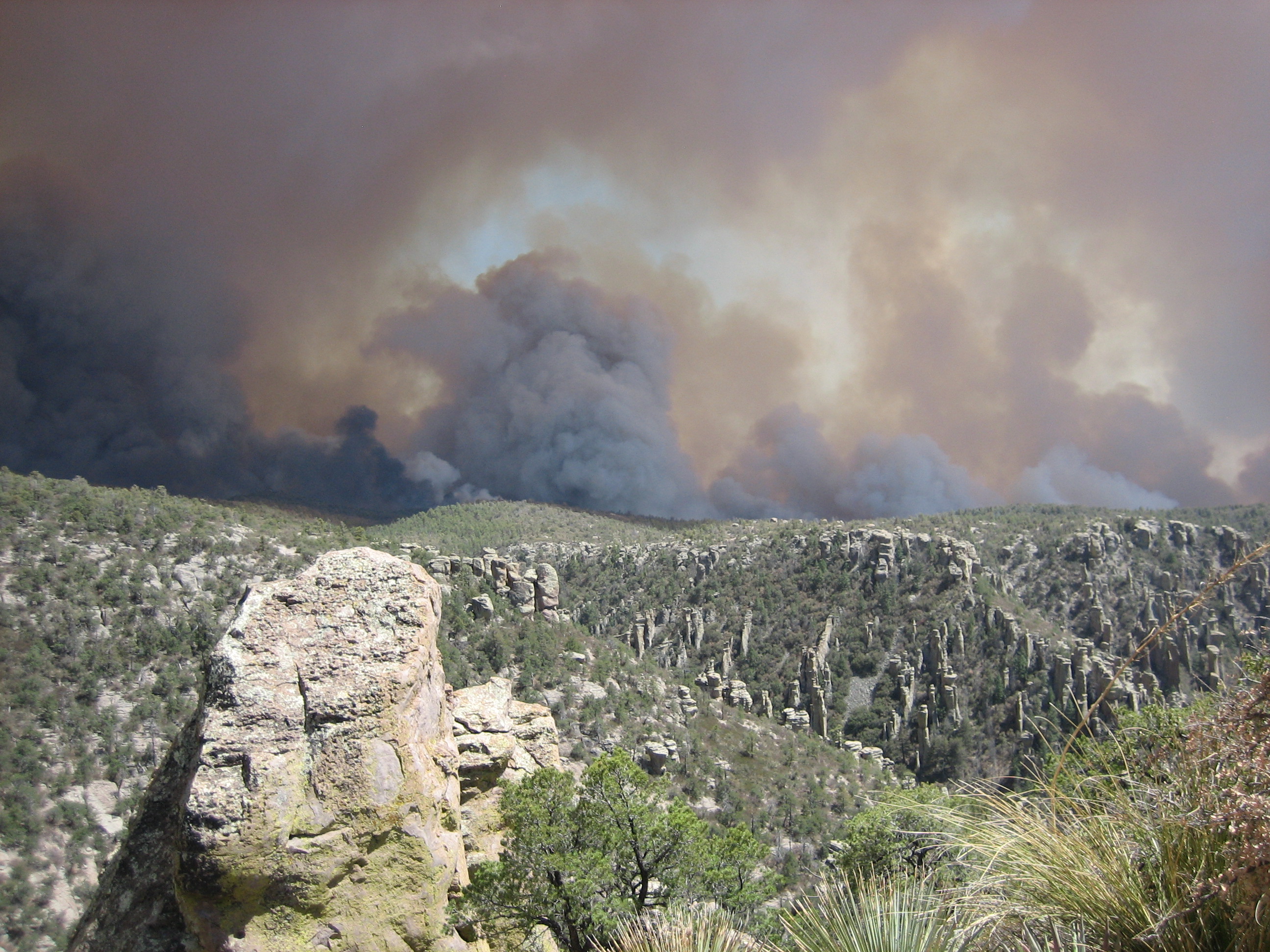 Billowing black, grey, and orange smoke over canyon filled with rock pinnacles.