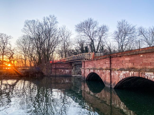A wood and steel bridge spans a red stone aqueduct with water below