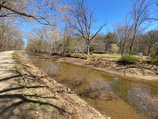 A watered canal with dirt banks and trees on either side