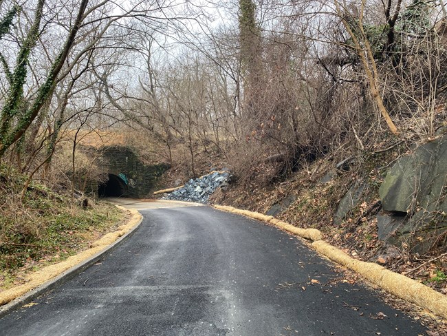 A paved road leads down to a historic stone culvert with vegetated banks on either side