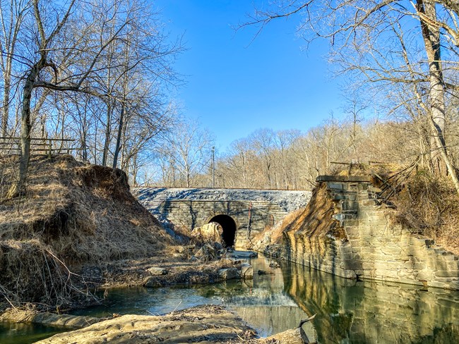 A body of water lays before masonry ruins left from a culvert and bridge that washed out.