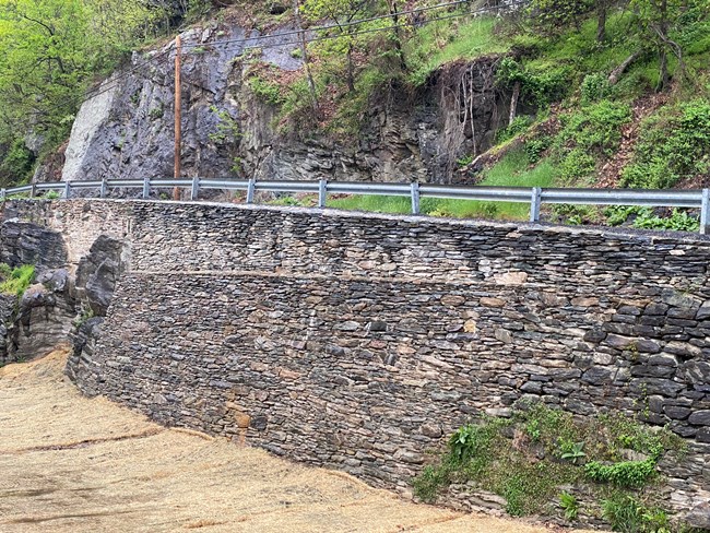 A large dry-laid stone wall holds up a paved road