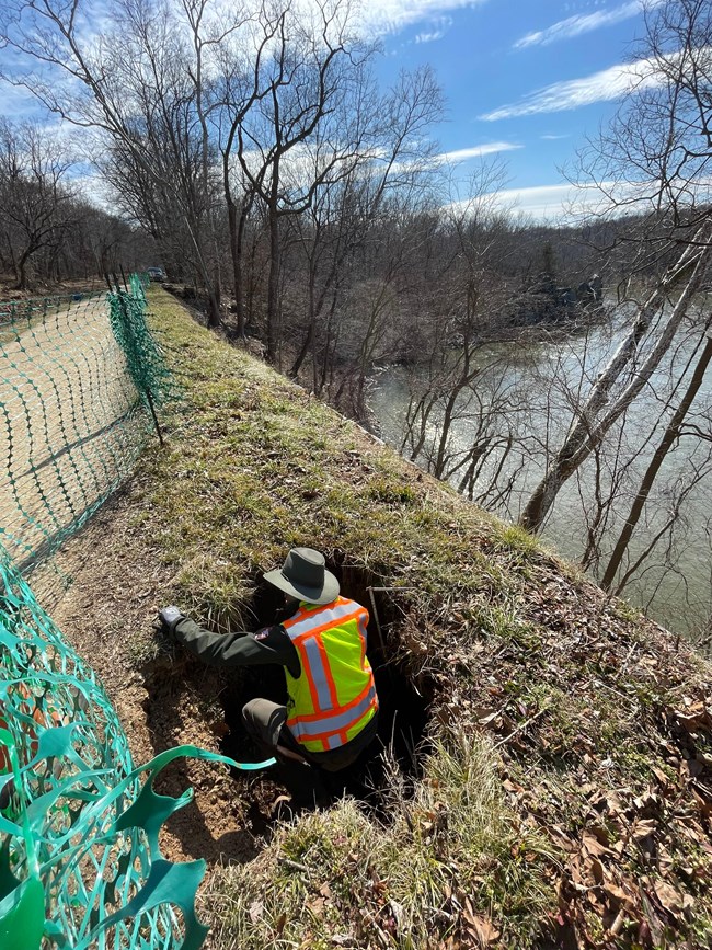 A park employee crouches in a large sinkhole along the edge of the bank