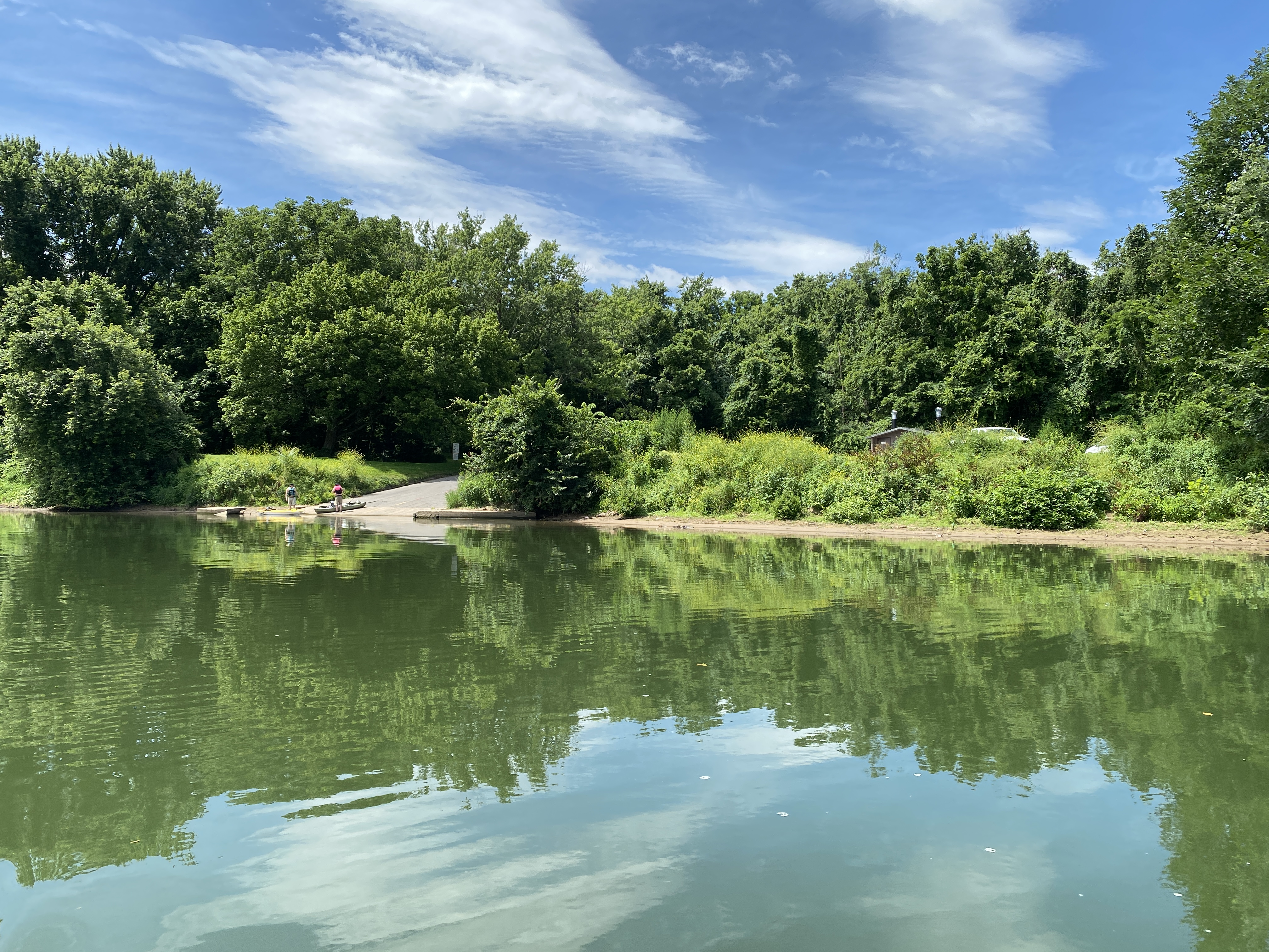 A concrete boat ramp sits along a vegetated river bank with the river in the foreground.