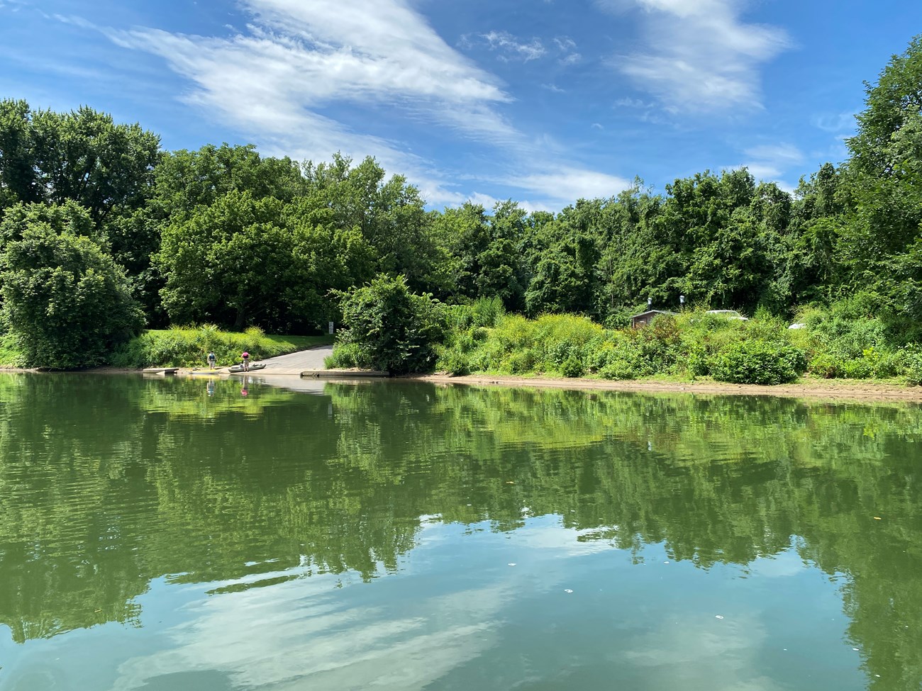 A concrete boat ramp sits along a vegetated river bank with the river in the foreground.