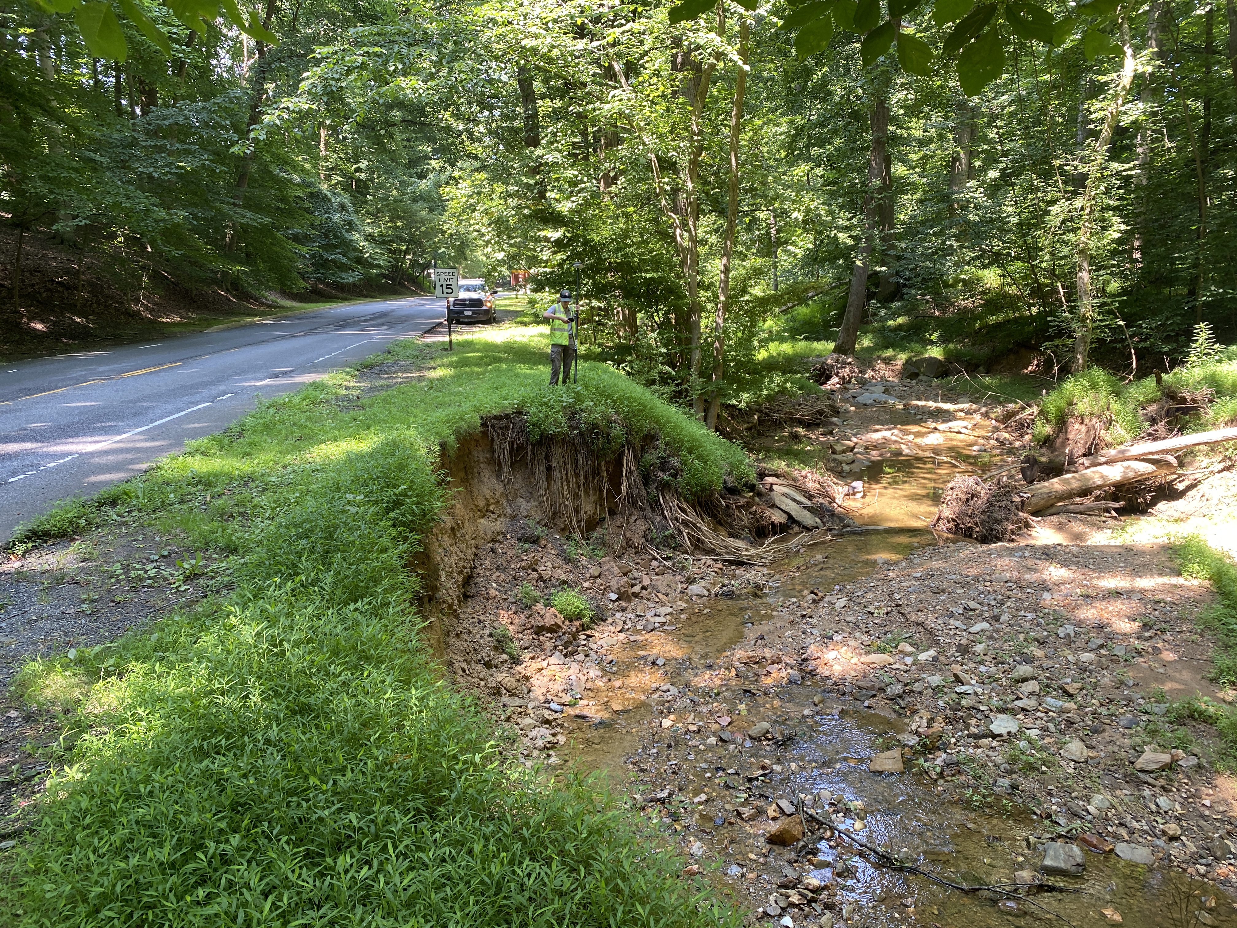 A stream causes bank erosion along a paved road.