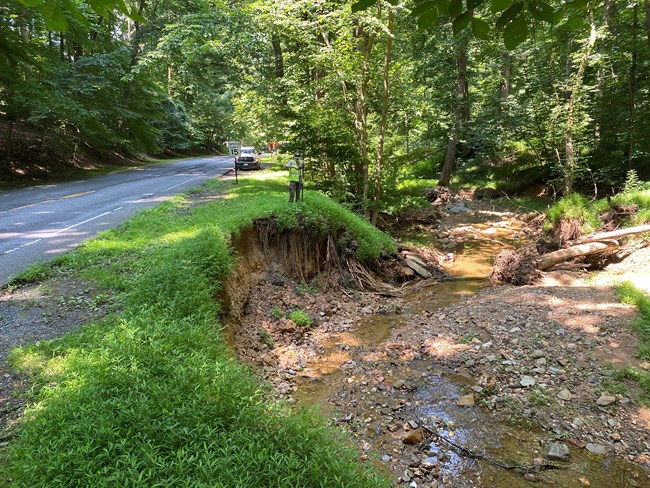 A stream causes bank erosion along a paved road.