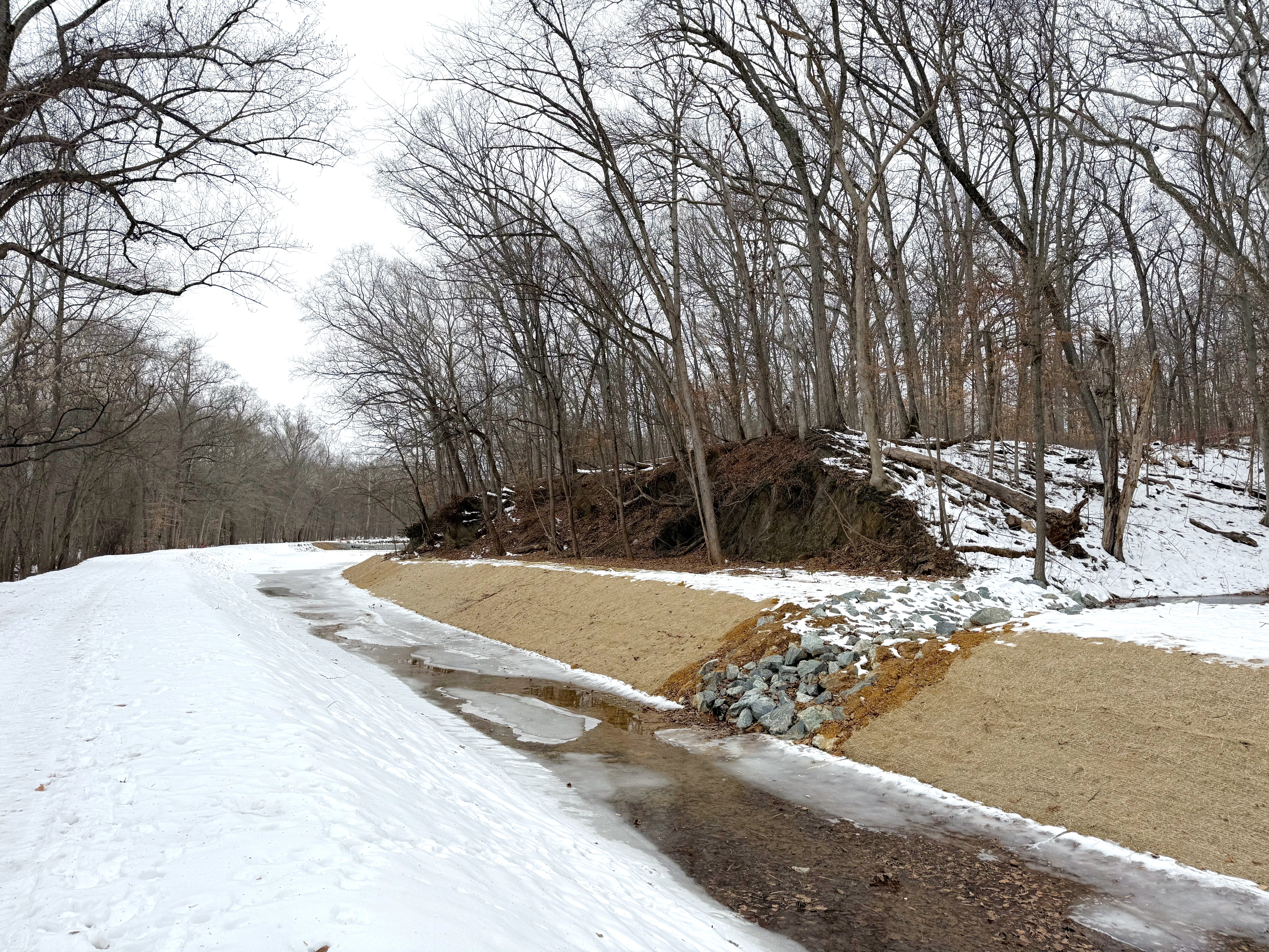 A canal with earthen embankments on either side, the foremost being covered in snow