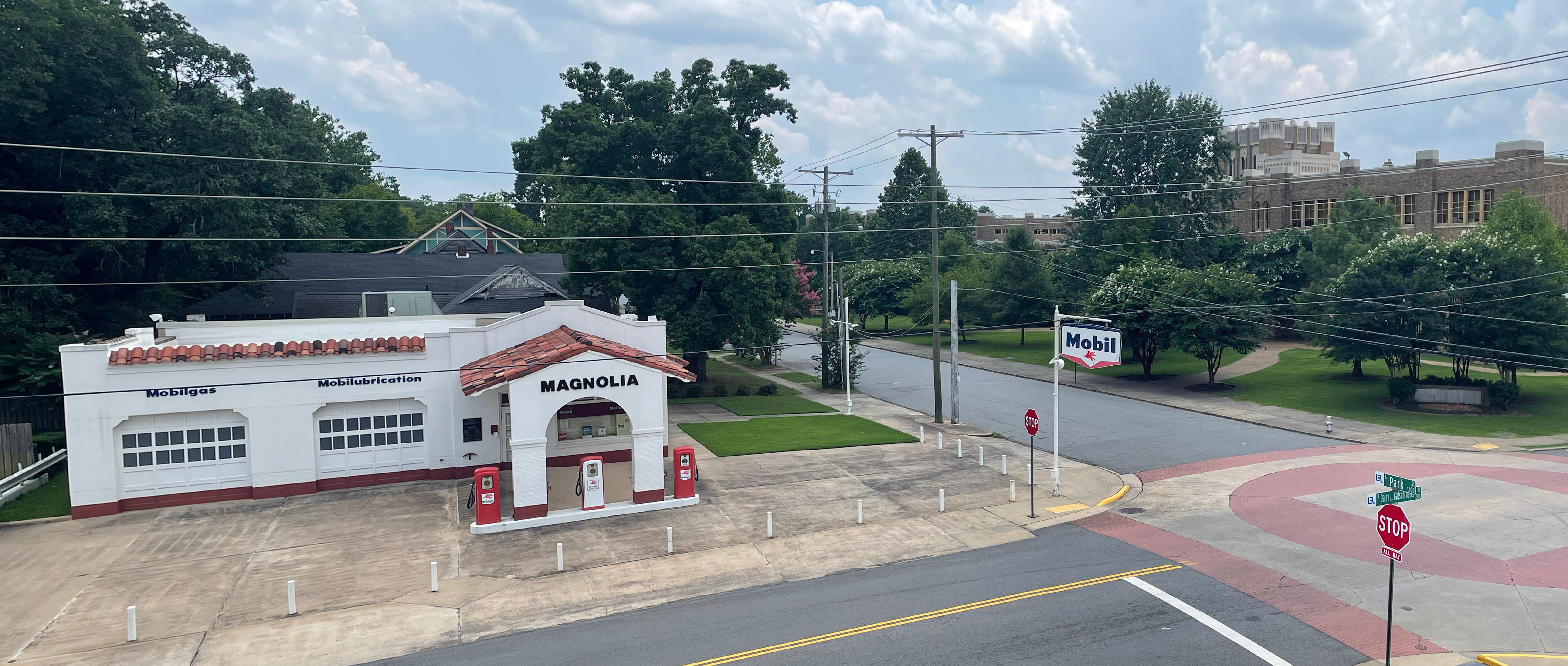 A restored historic Magnolia gas station with Mobil branding sits at the corner of Park and Daisy L. Gatson Bates Drive. The white stucco building features red-tile roofing and vintage gas pumps.