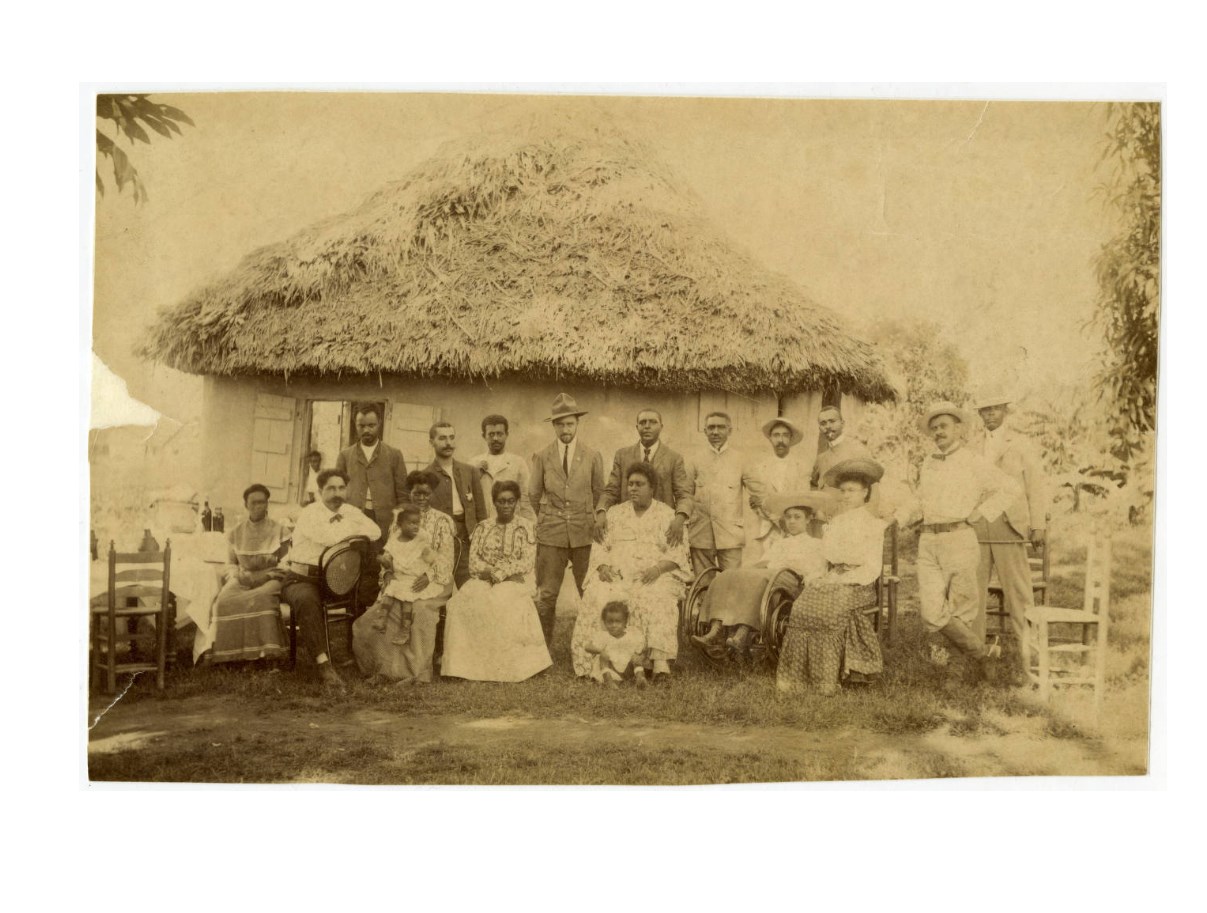 Black and white photo of Charles Young standing shoulder to shoulder with others looking directly at the camera. He is standing in the middle of the backrow of people. The first row is shoulder to shoulder sitting in chairs.