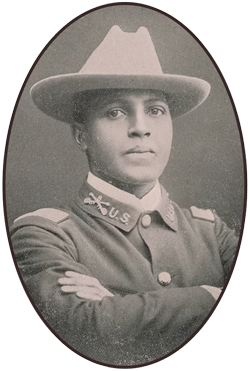 An African American soldier wearing a flat brim, light-colored hat with dark-colored blouse and his arms crossed at his chest