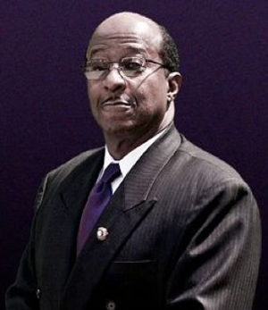 A man in a dark suit and purple tie wearing eyeglasses