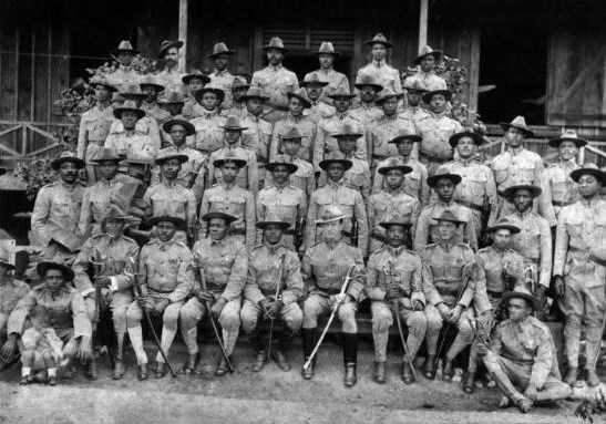 Several black Army soldiers standing and sitting while posing for a group portrait.