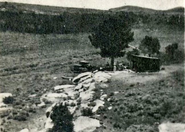 Grainy black and white photo where a building with an old truck parked out front is situated among rocks and juniper trees in what is now City of Rocks.
