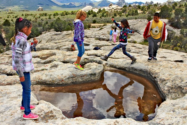 Kids in City of Rocks on a rock slab with water filled panhole formations.