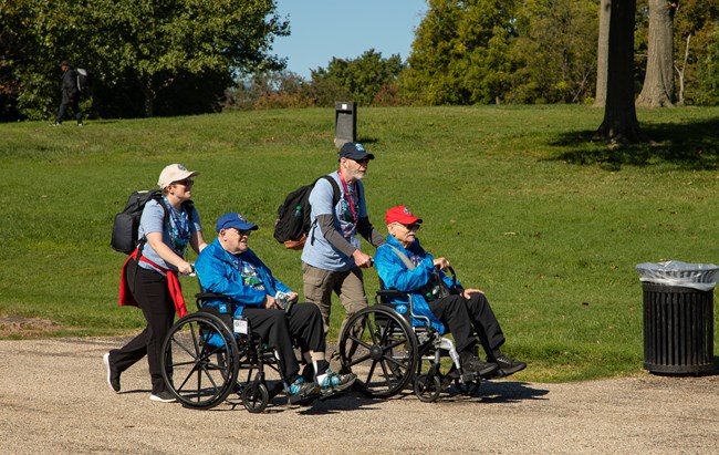 Two individuals in a wheelchair are each lead side by side through Constitution Gardens.
