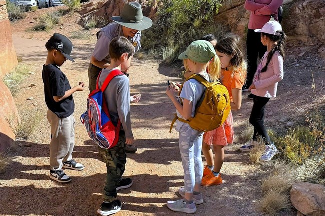 young students stand in circle as ranger helps with observation of rocks